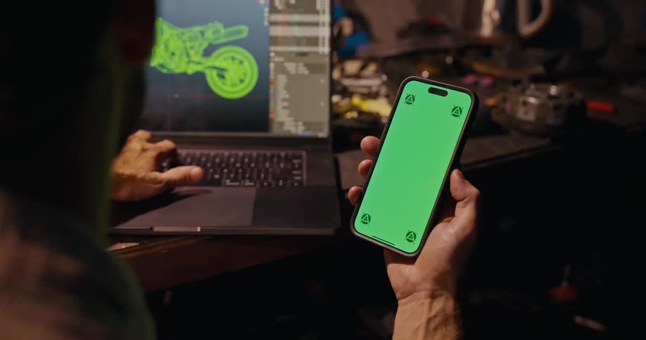 Man views smartphone while manipulating motorcycle drawing on a laptop screen