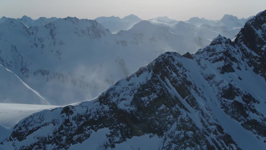 A range of snow capped mountains stretches into the distance with a cloudy sky above