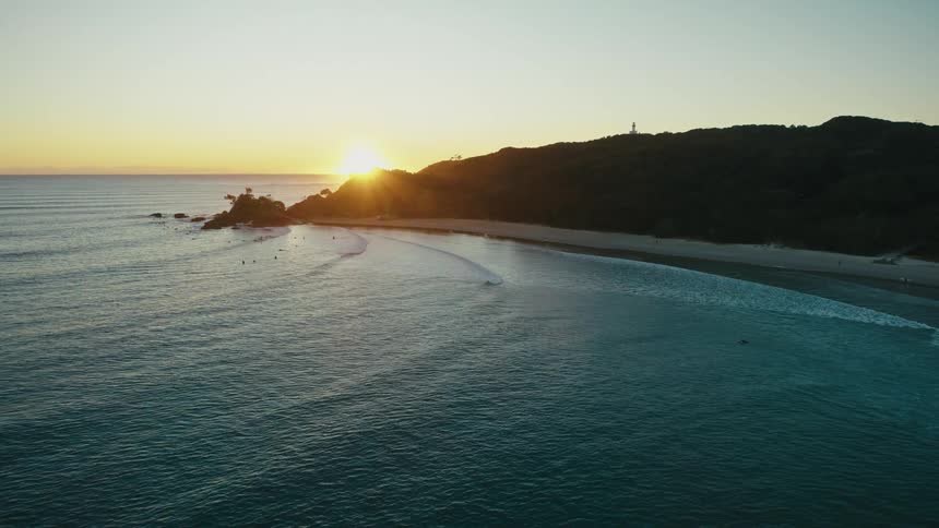 Beach side promontory blocks the sight of the sun sitting on the red tinted horizon