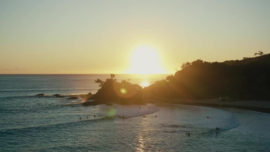 Aerial of a group of people surfing ocean waves at sunset