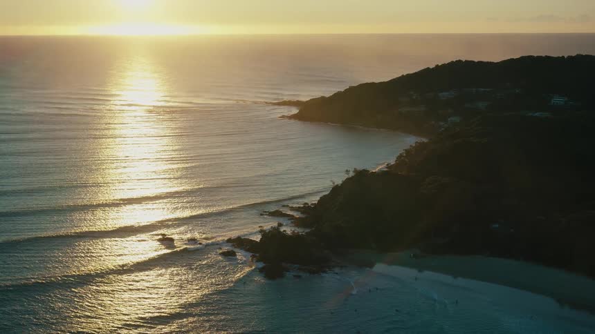 An aerial view of a golden sunrise over a secluded beach with a rocky headland