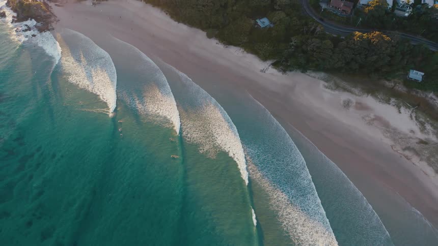 Waves roll onto the beach near the highway passing through the forest enclosing a coastal town