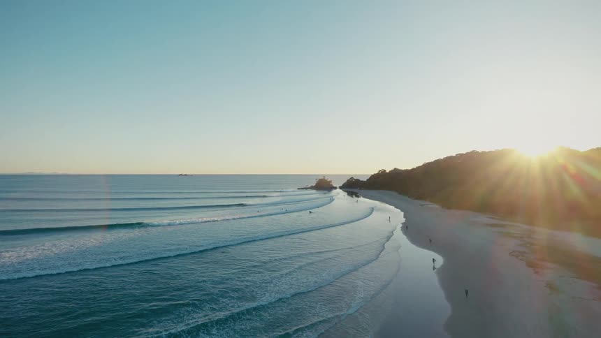 Aerial view of the sun setting over a coastal landscape casting long shadows over the beach and the ocean waves