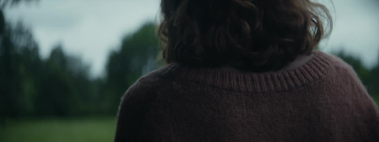 Woman walks across a field bordered by the woods