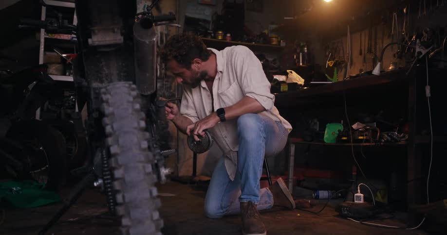 A person kneels in a workshop working on the rear wheel of a motorcycle