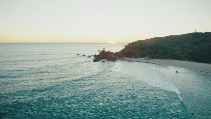 The sun dips below the horizon casting a warm glow on the beach as surfers ride the waves and swimmers cool off in the crystalclear water