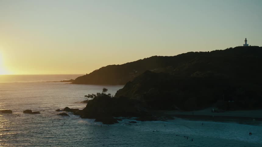 Aerial view of the sun setting over a coastal landscape casting long shadows over the beach and the ocean waves