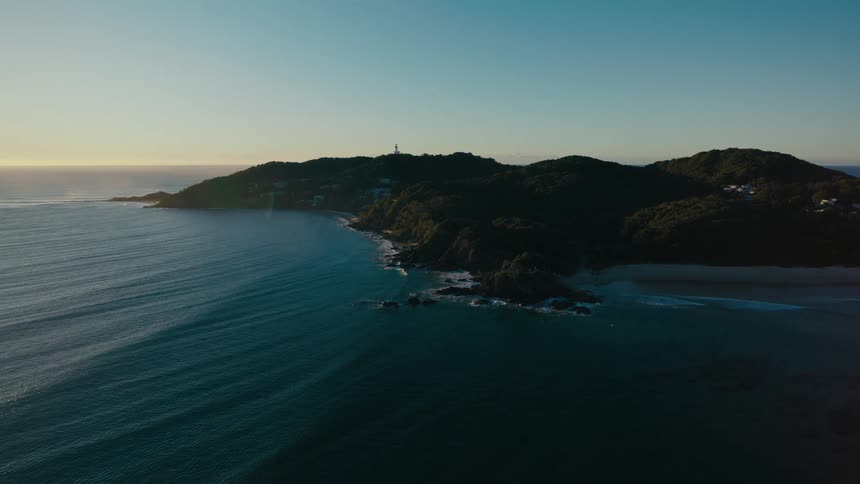 A tranquil tree covered headland juts out into a calm blue ocean
