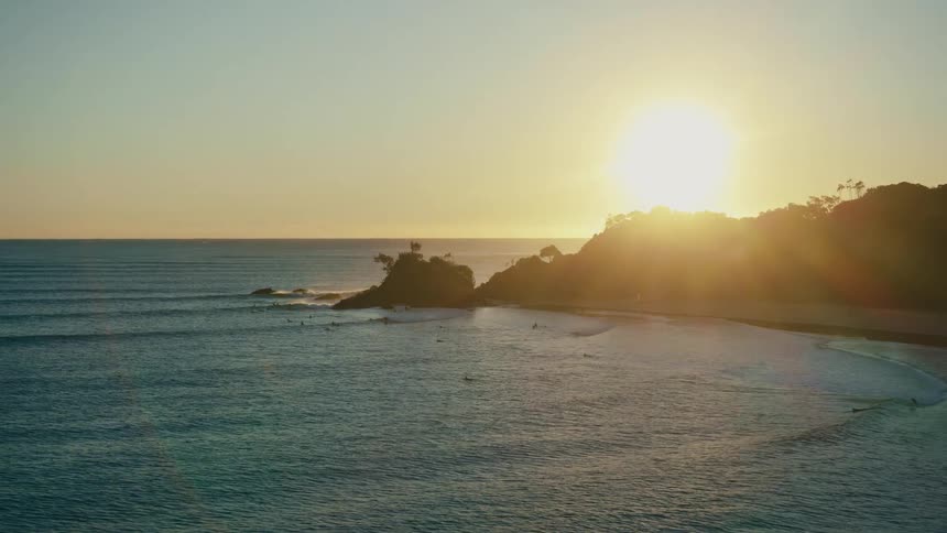 A serene coastal scene at dusk with rolling waves gently lapping against the sandy shore while the sun casts a warm glow over the distant hills