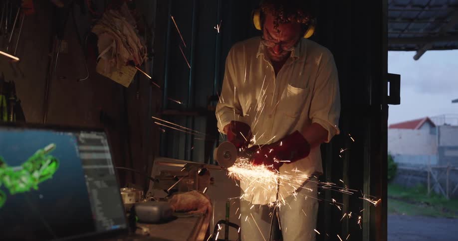 A person uses a grinder producing sparks in a dimly lit workshop