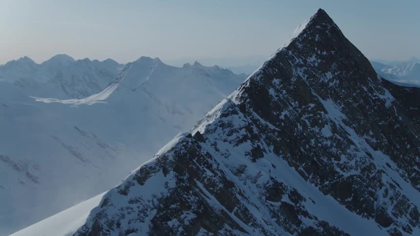 A sharp snowcapped mountain peak rises above a range of other snow covered mountains