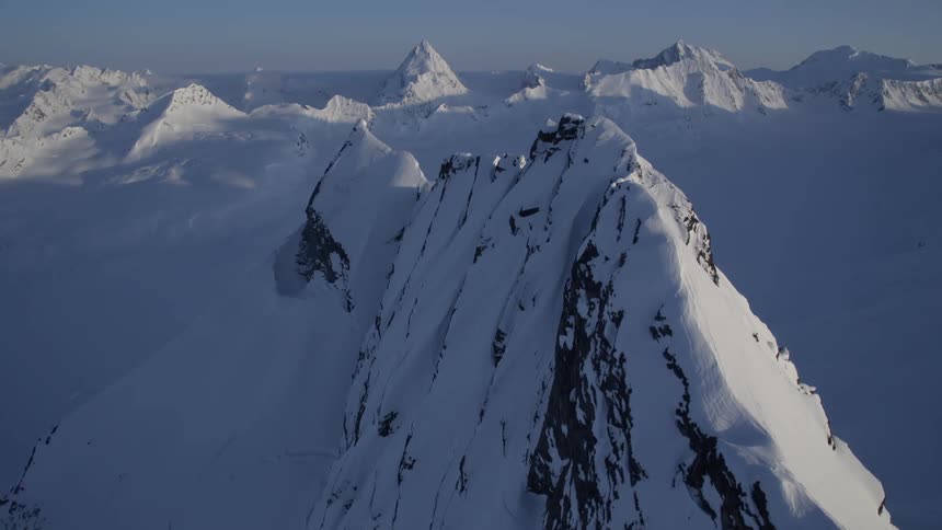 The sun casts a golden glow on a snowcapped mountain peak while the surrounding landscape is blanketed in a pristine layer of white