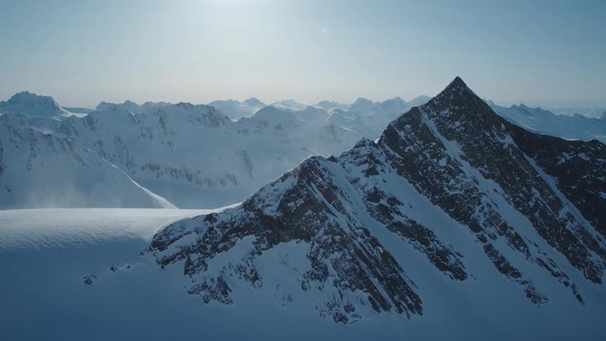 A snow covered mountain range with sharp peaks and ridges is shown under a clear sky