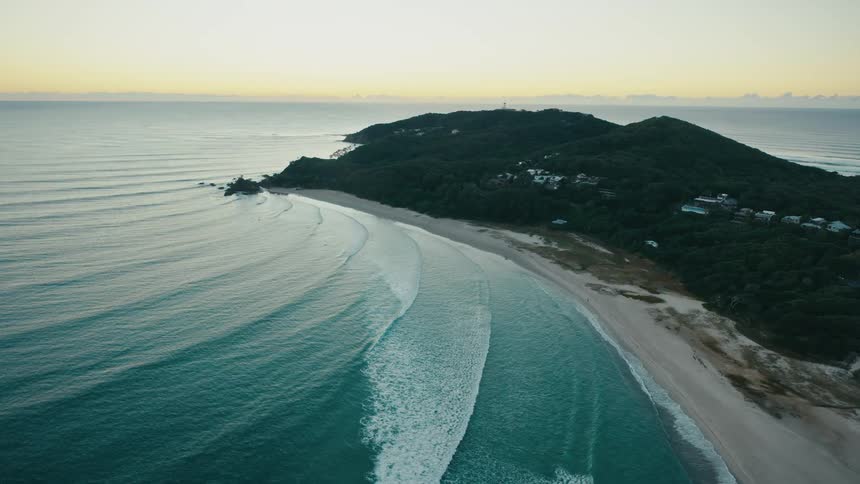 Large waves crash against a beach near a rural community