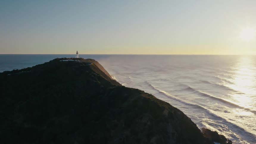 A lighthouse sits atop a cliff overlooking the ocean at sunset