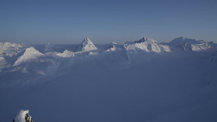 A vast expanse of snowcapped mountains stretches across the horizon under a clear blue sky