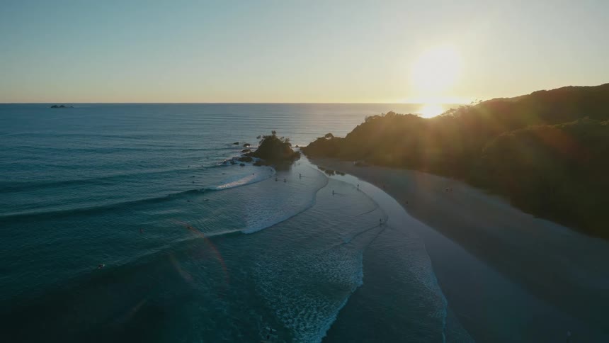 Aerial of a group of people running on the beach and swimming in the ocean at sunset