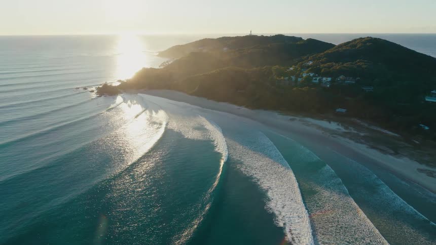 Aerial view of a beach with the coast in the background and the morning sun
