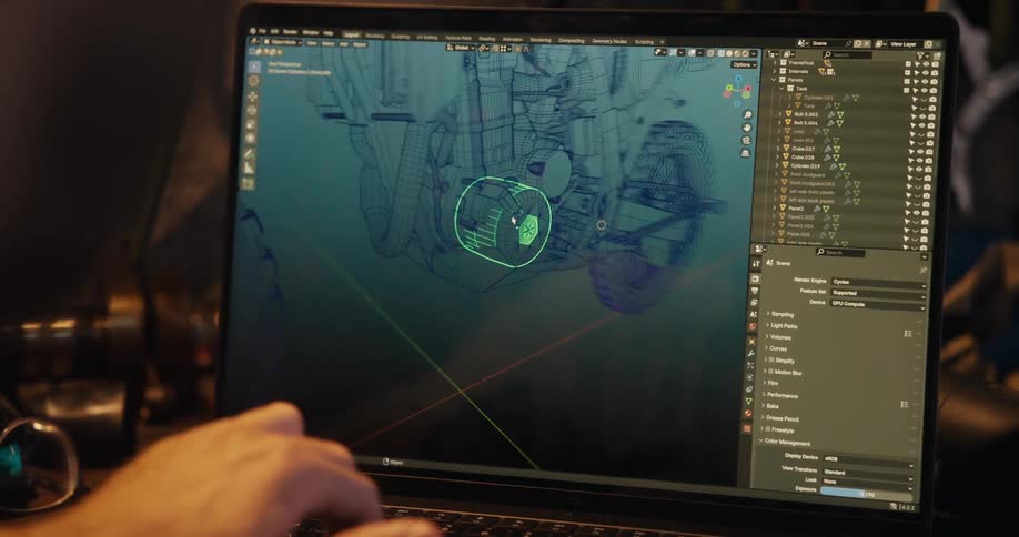 A man works on a laptop in a workshoplike setting using 3d modeling software displaying a complex mechanical structure with wireframes and multiple layers