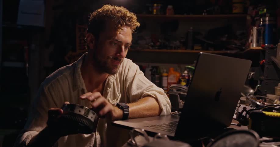 Man holding a cylindrical part of a motorcycle and working on a laptop