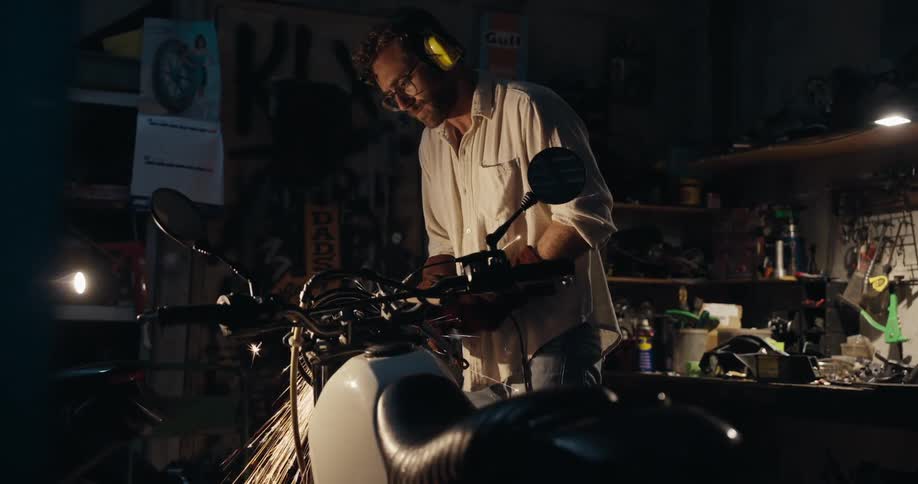 A person wearing safety glasses and ear protection works on a motorcycle in a dimly lit workshop