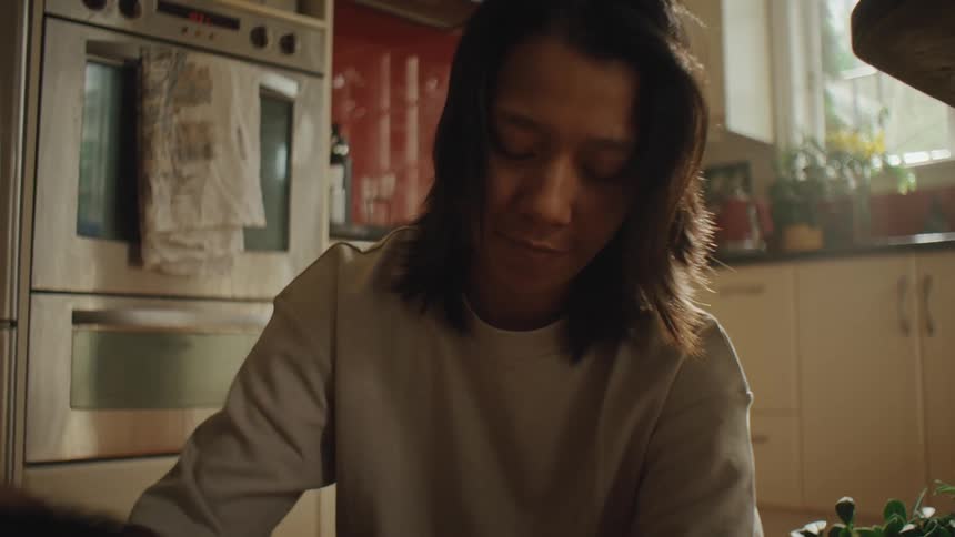Woman with straight hair and a silver sweater pets her dog in the kitchen near the oven
