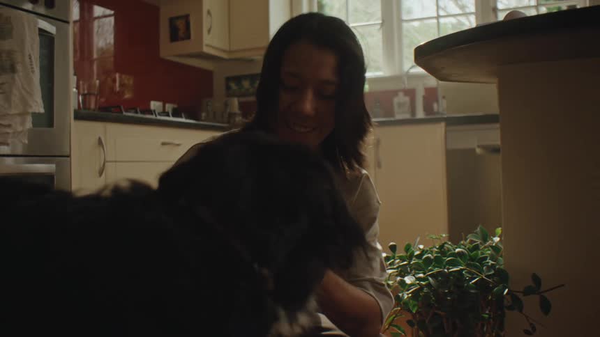 A woman feeds and pets her dog on the kitchen floor at home