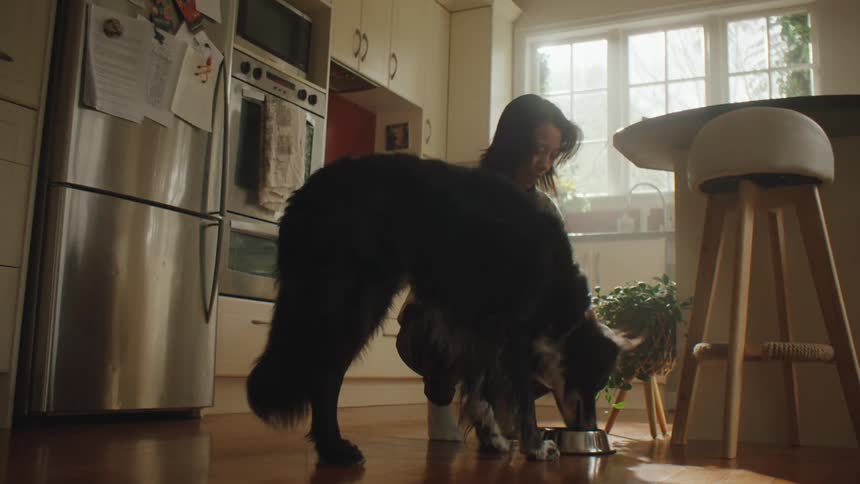 A woman feeds and pets her dog on the kitchen floor at home