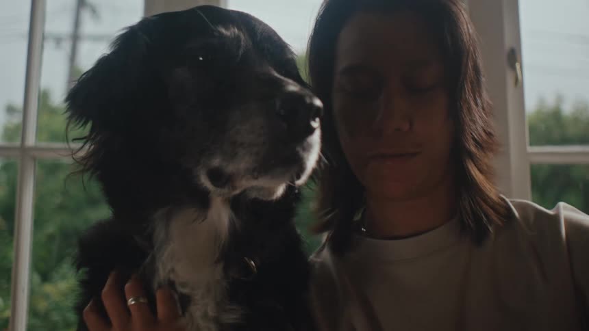 A woman takes a selfie while petting a dog sitting by a window at home