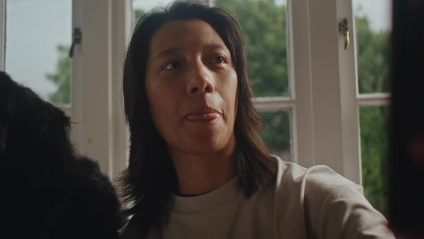 A woman takes a selfie while petting a dog sitting by a window at home