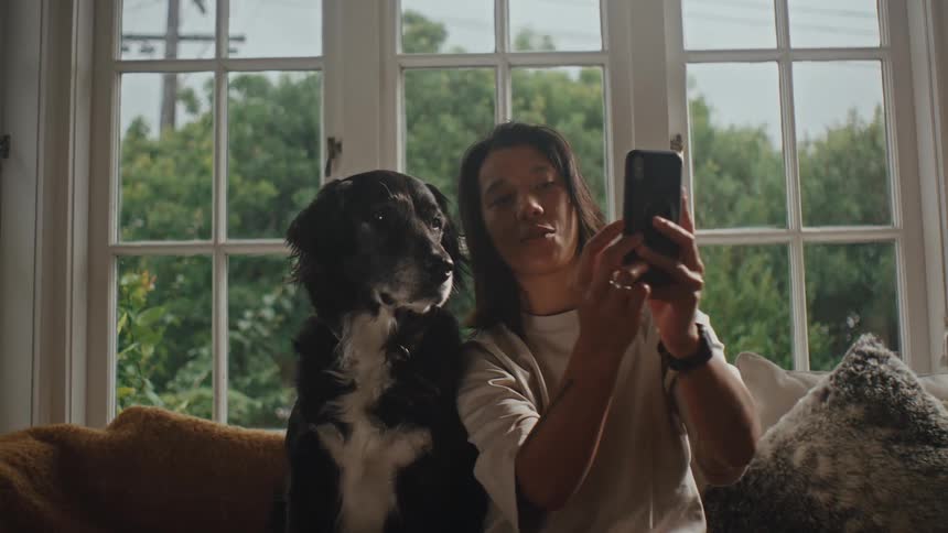 Person interacting with a smartphone and next to a dog sitting on a sofa