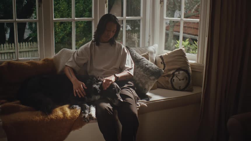An asian woman sits on a couch petting a dog