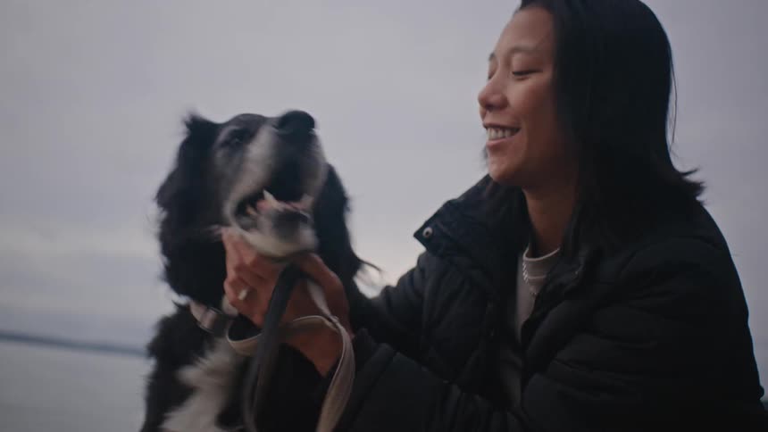 Woman pets her dog in front of the ocean