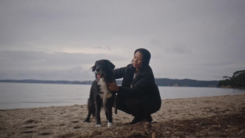 Woman crouching on the sand at the beach petting her dog