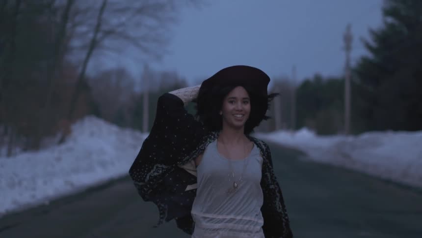 Woman holding her hat on runs down a road at sunset