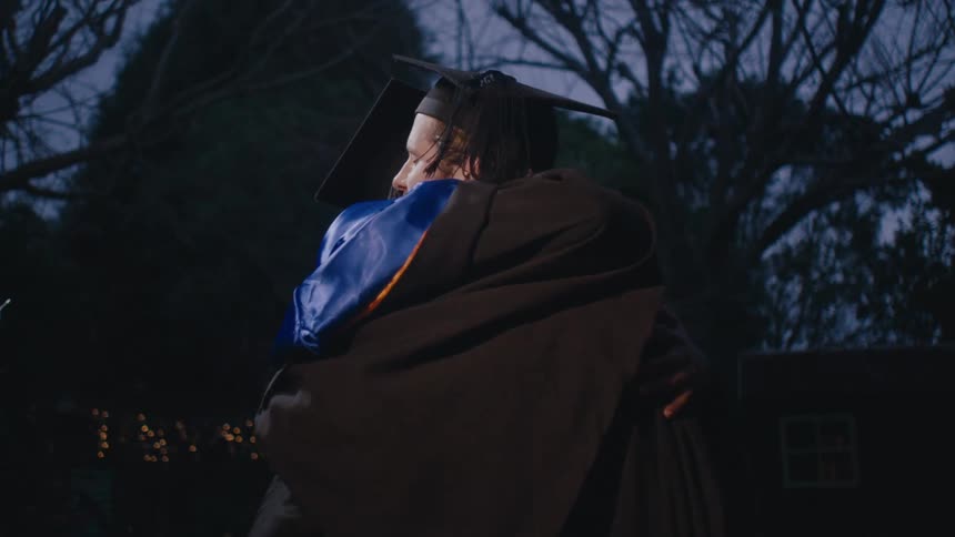 Two graduates in academic robes and caps hug each other in a celebration