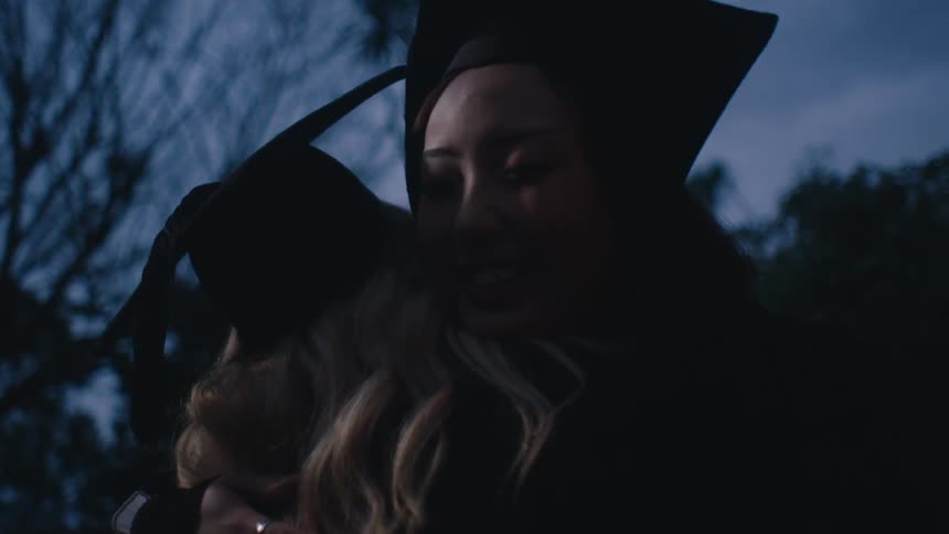 A group of people in graduation gowns and caps celebrate by hugging each other