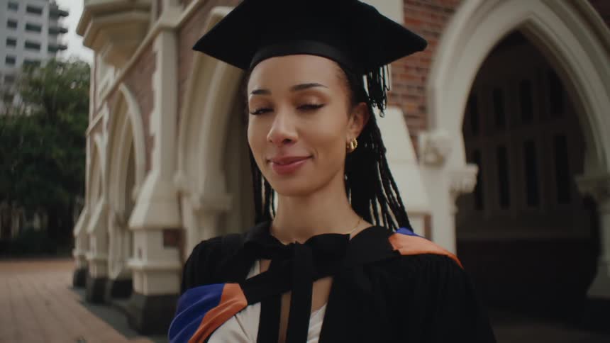 Female graduate poses in her robe and cap near a campus building