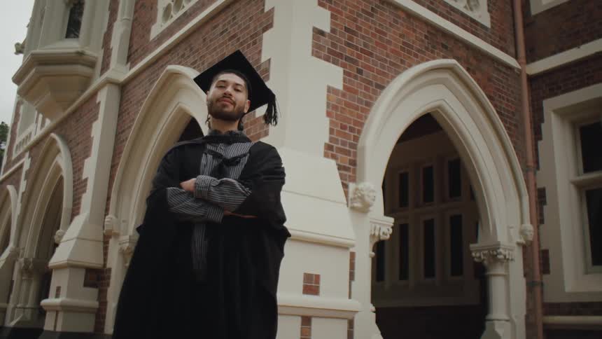 Graduate crosses his arms and smiles in his academic wear