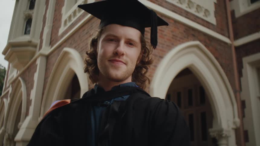 A person with long wavy blonde hair wearing a black academic cap and gown