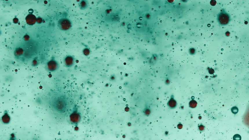 A swirling mass of turquoise liquid is speckled with dark almost black spherical orbs creating a mesmerizing otherworldly pattern