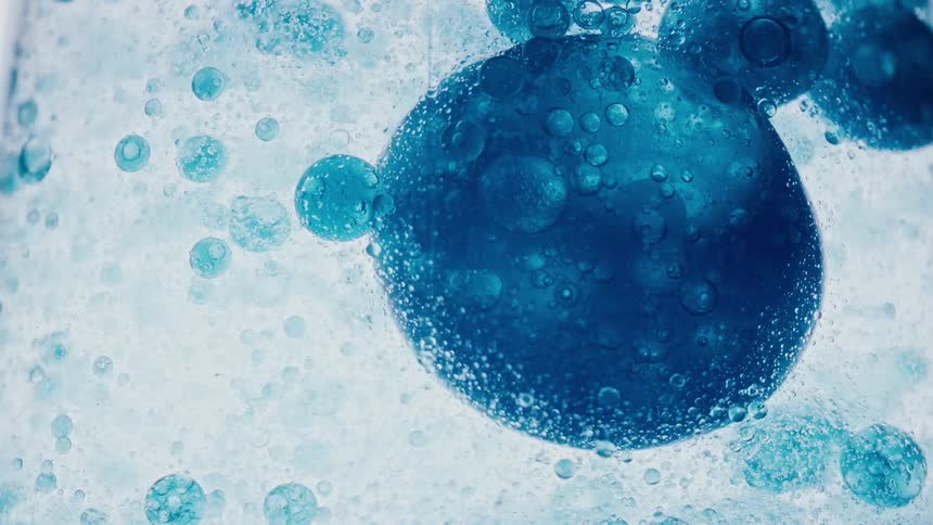 Close up of large bubbles of blue ink floating down a clear liquid