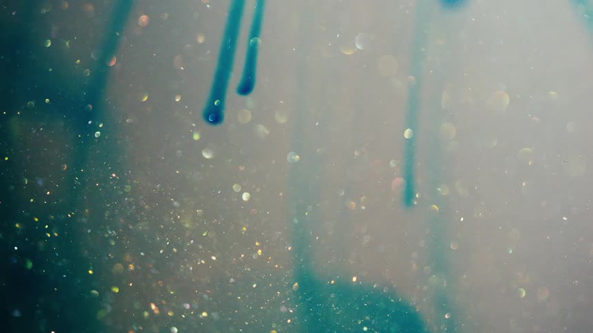 A blue liquid swirls with specks of glittering particles floating over