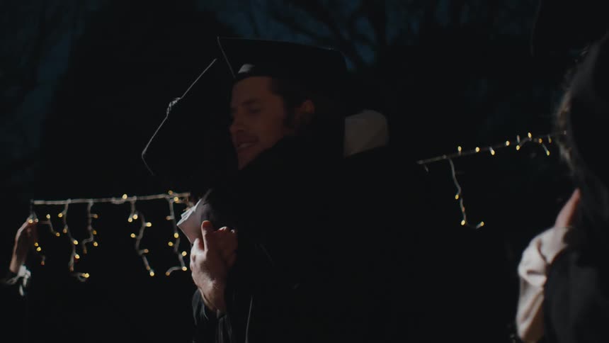 An older woman watches two students who just graduated hug each other