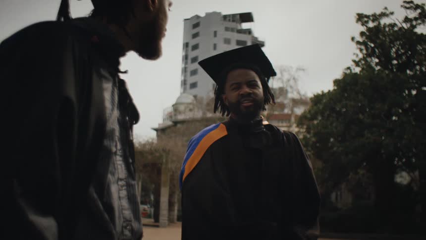 A group of people in graduation gowns and caps gather outdoors to talk