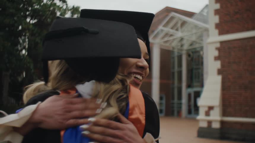 Friends in graduation gowns and caps celebrate by hugging each other