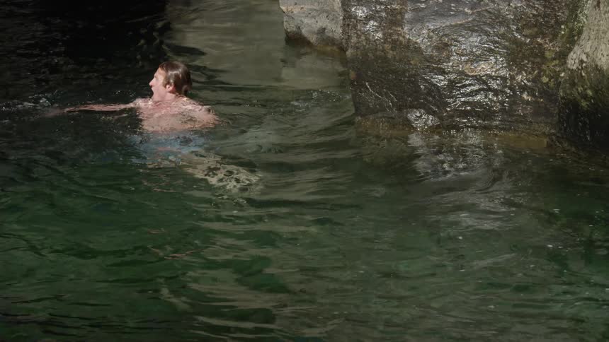 A man surfacing from under the water located next to large rocks
