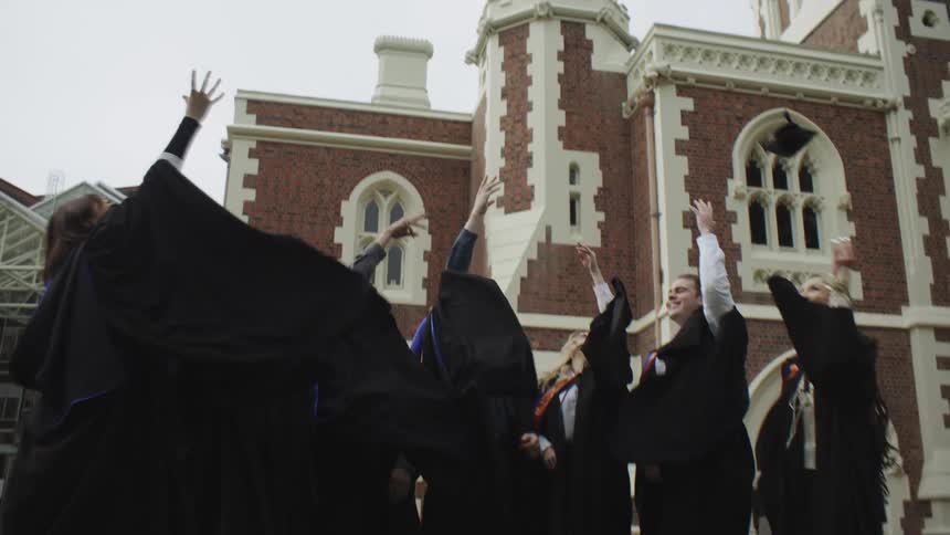 A group of people in graduation gowns and caps celebrate by throwing their caps in the air