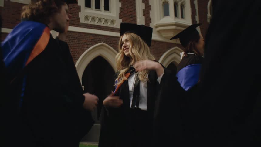 A group of people in graduation gowns and caps talking near a university or college building