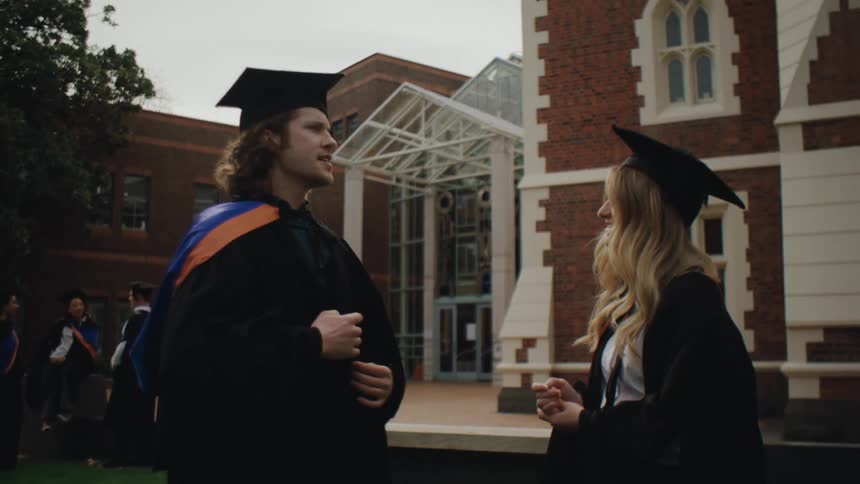 Man and woman in graduation gowns talking on a campus